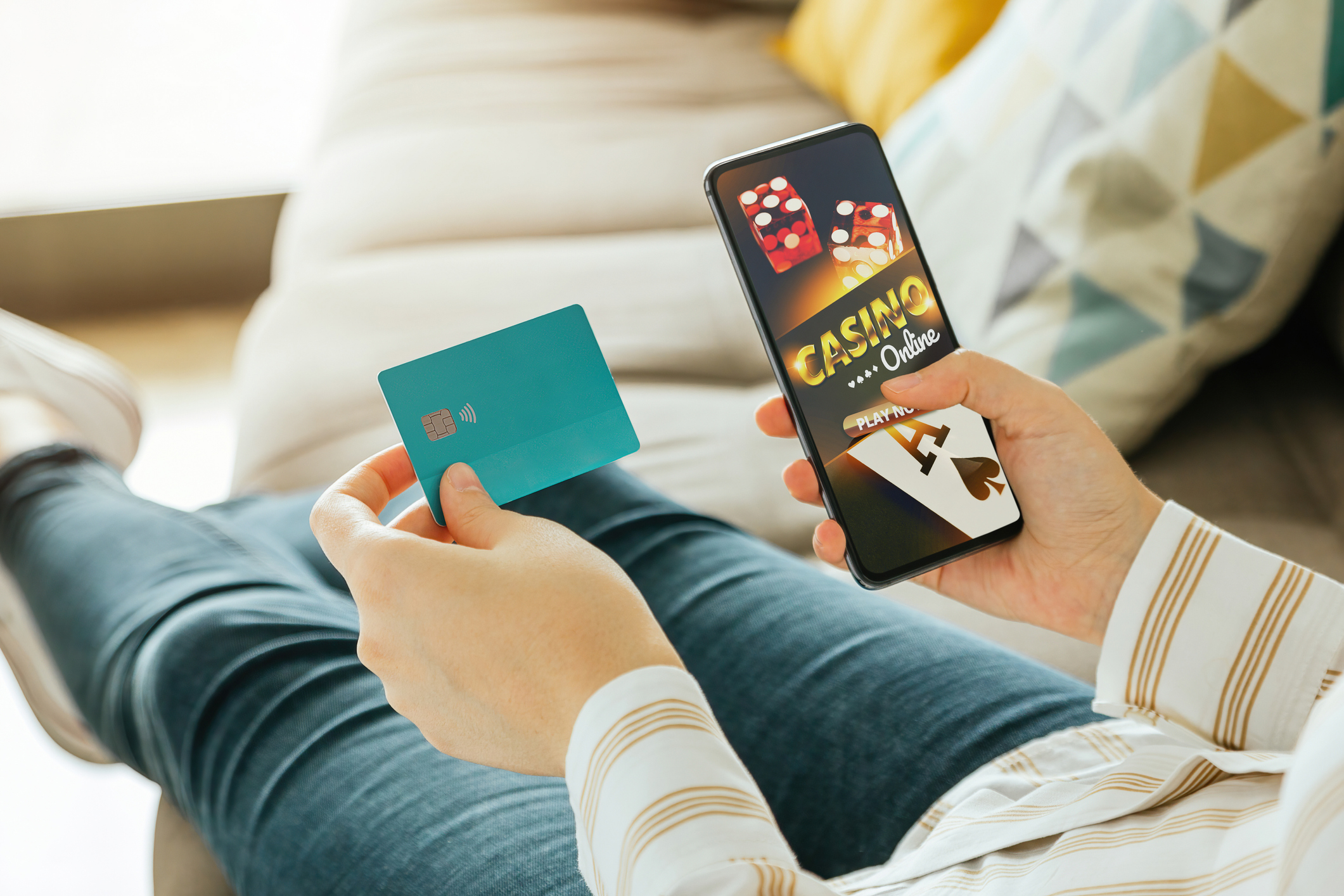 A person holds credit card in left hand and phone with gaming app in right hand.