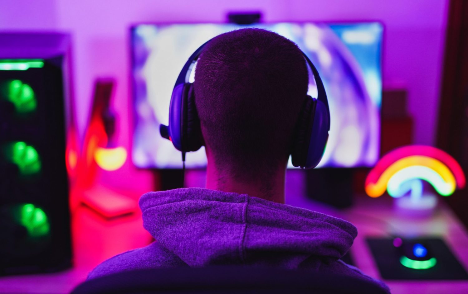 A person wearing head phones and looking at a computer screen, viewed from behind.