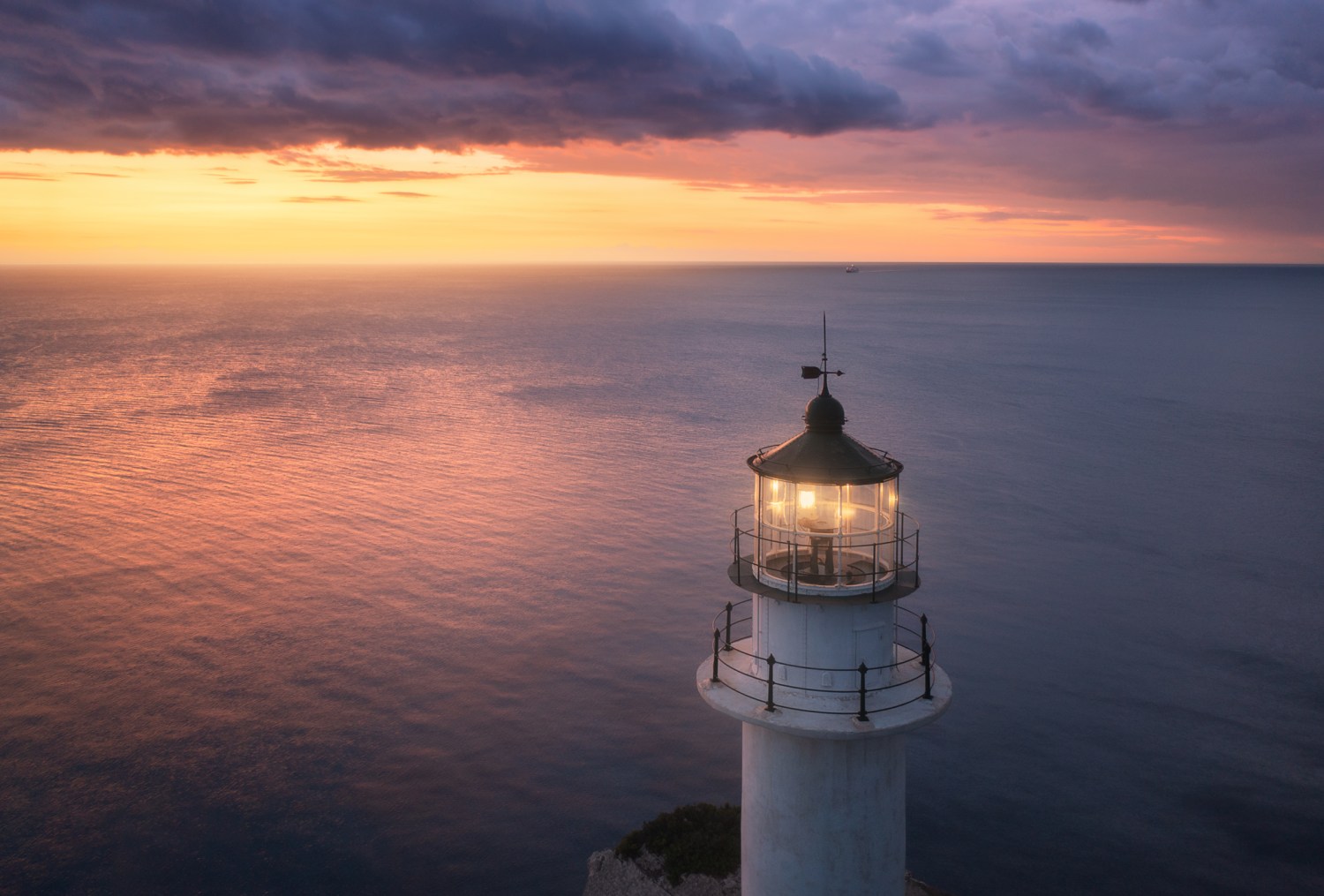 A lighthouse illuminates the water against a sunset background.