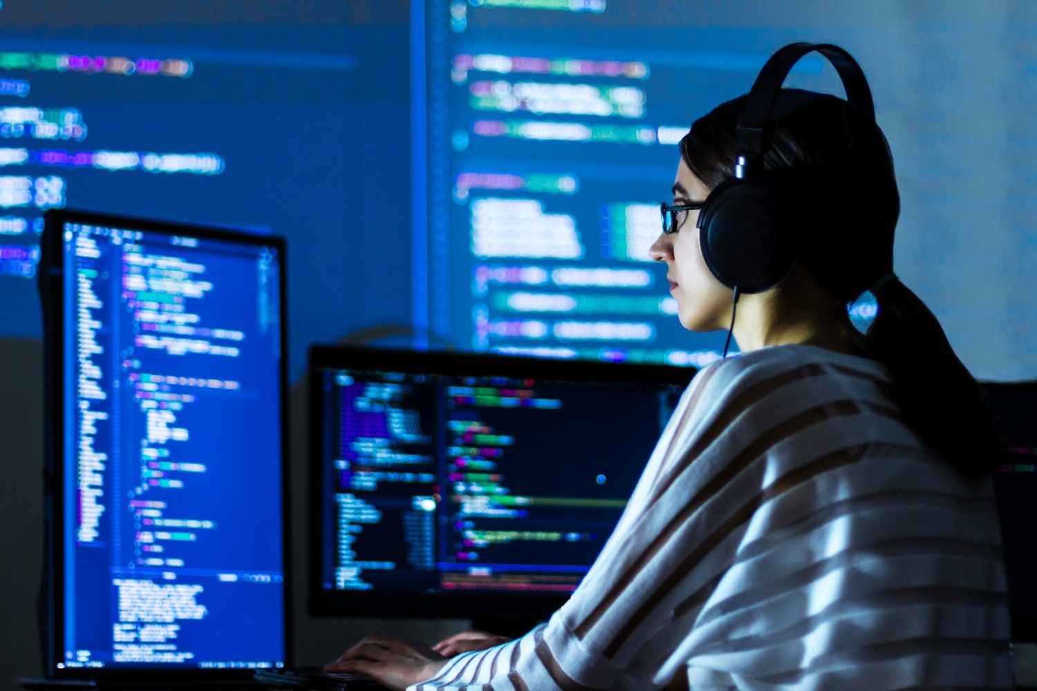 Software developer freelancer woman female in glasses work with program code C++ Java Javascript on wide displays at night