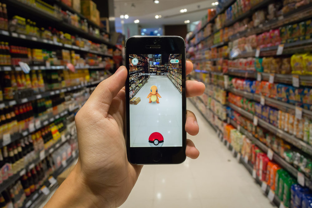 A hand holds a smartphone showing Pokemon GO game in a supermarket aisle.