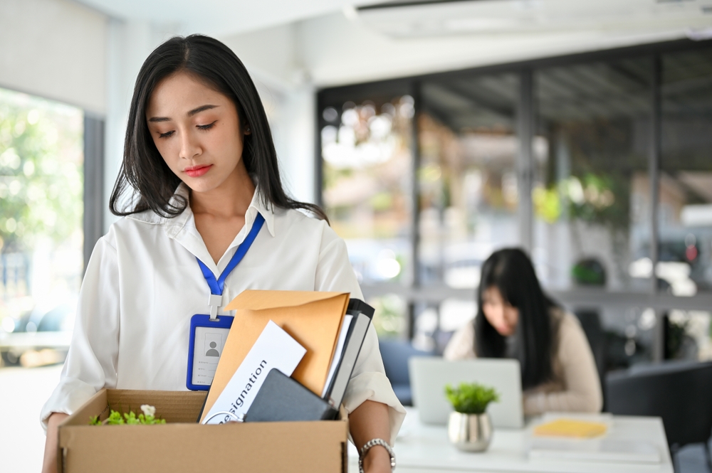 A person carries a box of personal belongings from an office where they have been laid off from.