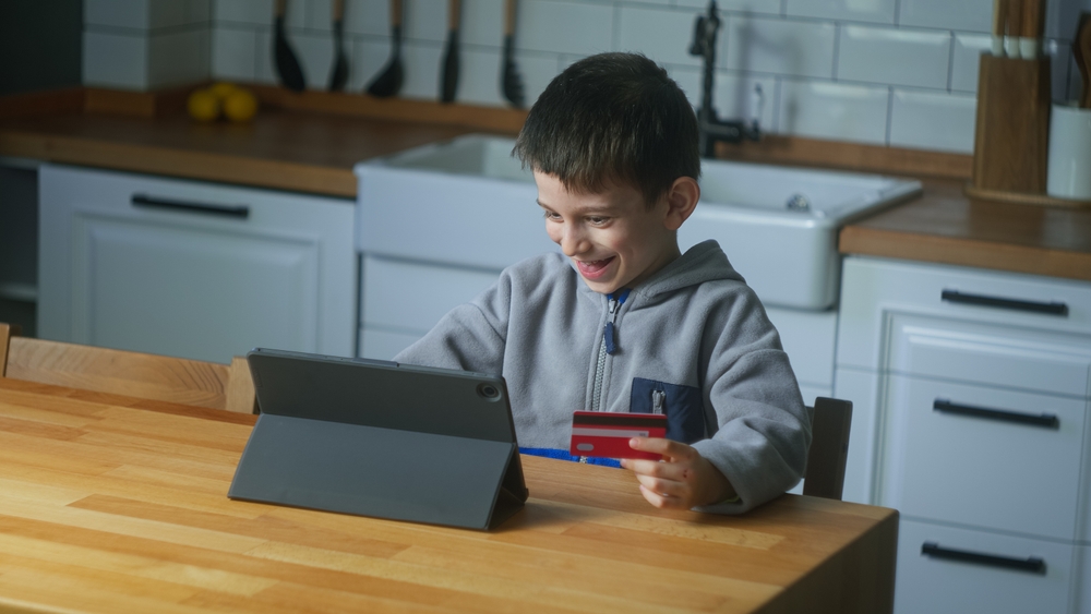 Young person on computer holding a credit card, theoretically to make a purchase.